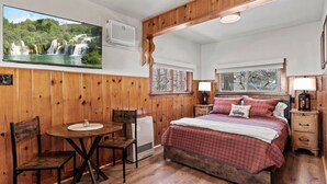 A bedroom with a wooden bed, a small table, chairs, and a TV displaying a waterfall. - Timber Lodge Cabin #6 (Colorado Springs)