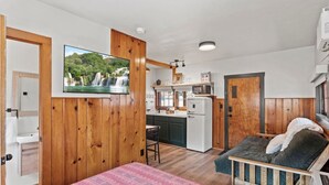A cozy room with a bed, a wooden wall, a TV, a kitchen area with a fridge and microwave, and a bathroom with a sink and toilet. - Timber Lodge Cabin #8 (Colorado Springs)
