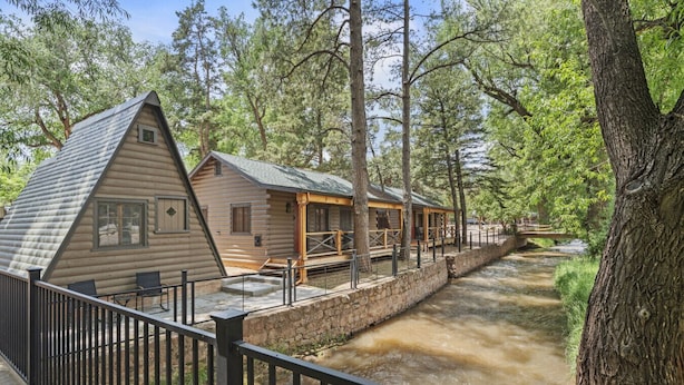 A log cabin-style building with a porch and a stone wall alongside a river. - Timber Lodge Cabin #8 (Colorado Springs)