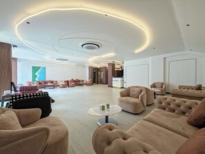 Een moderne hotel lobby met zachte zitplaatsen, een receptiebalie en een groot abstract schilderij aan de muur.