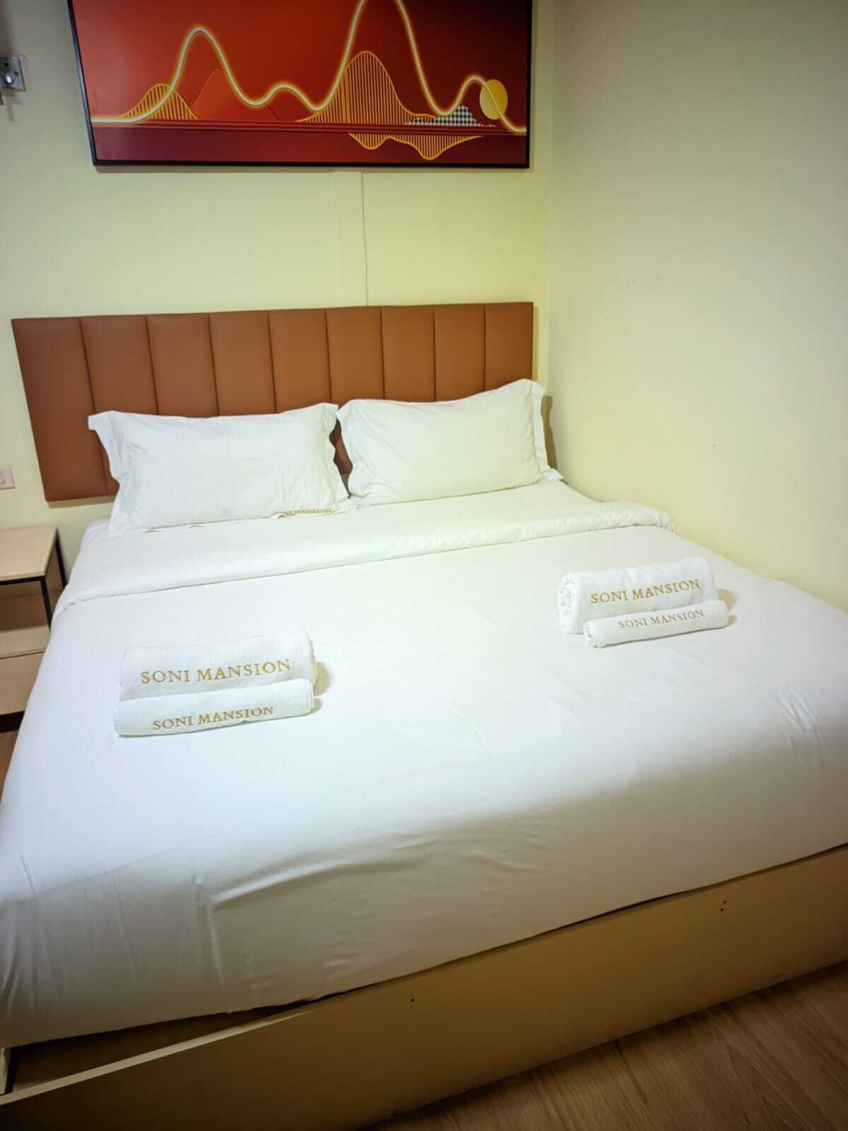 A hotel room with a bed, pillows, and a headboard. There is a wall art piece above the bed.