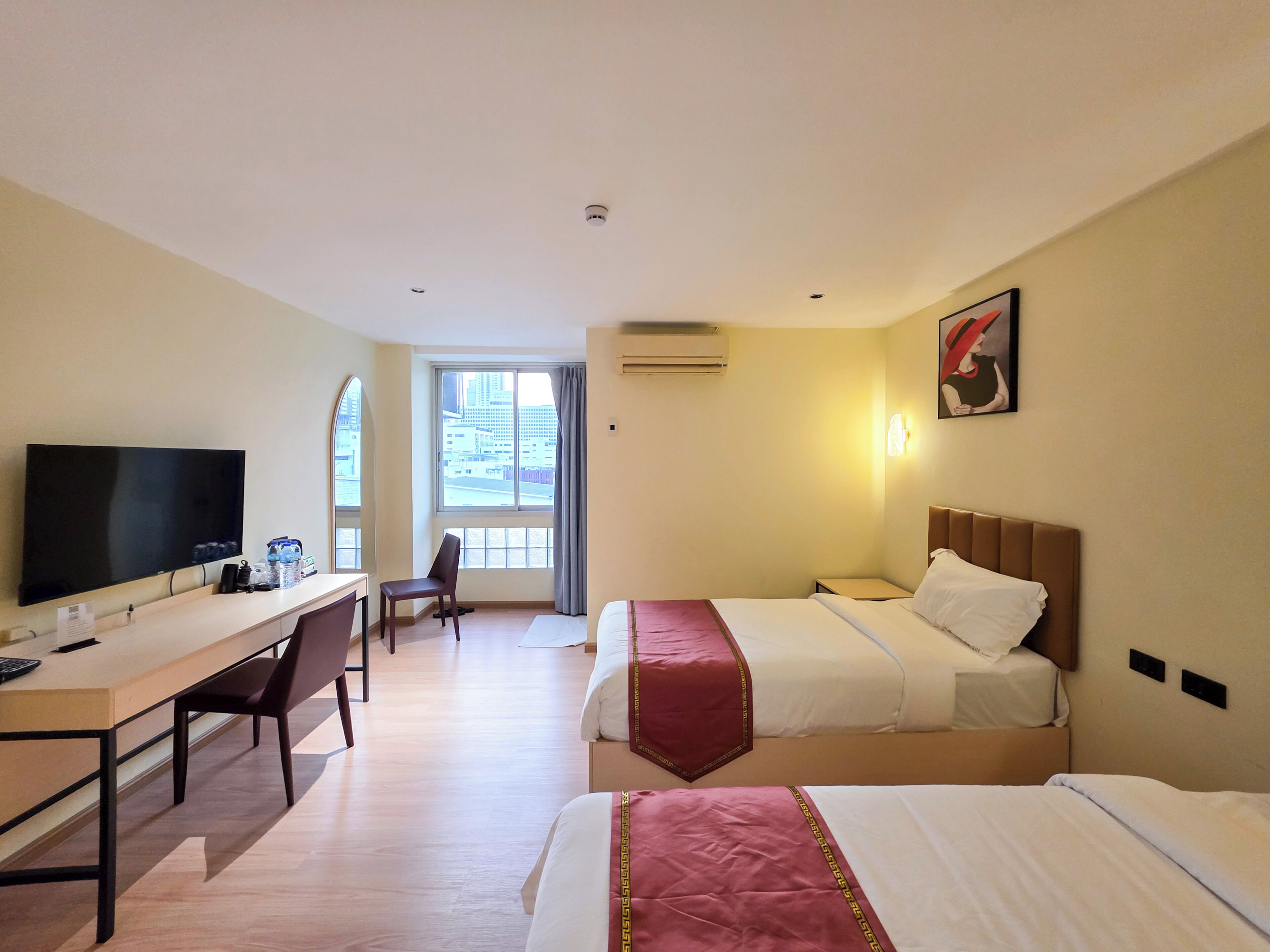 Een hotelkamer met een bed, een bureau, een stoel, een televisie en een raam met uitzicht op gebouwen.