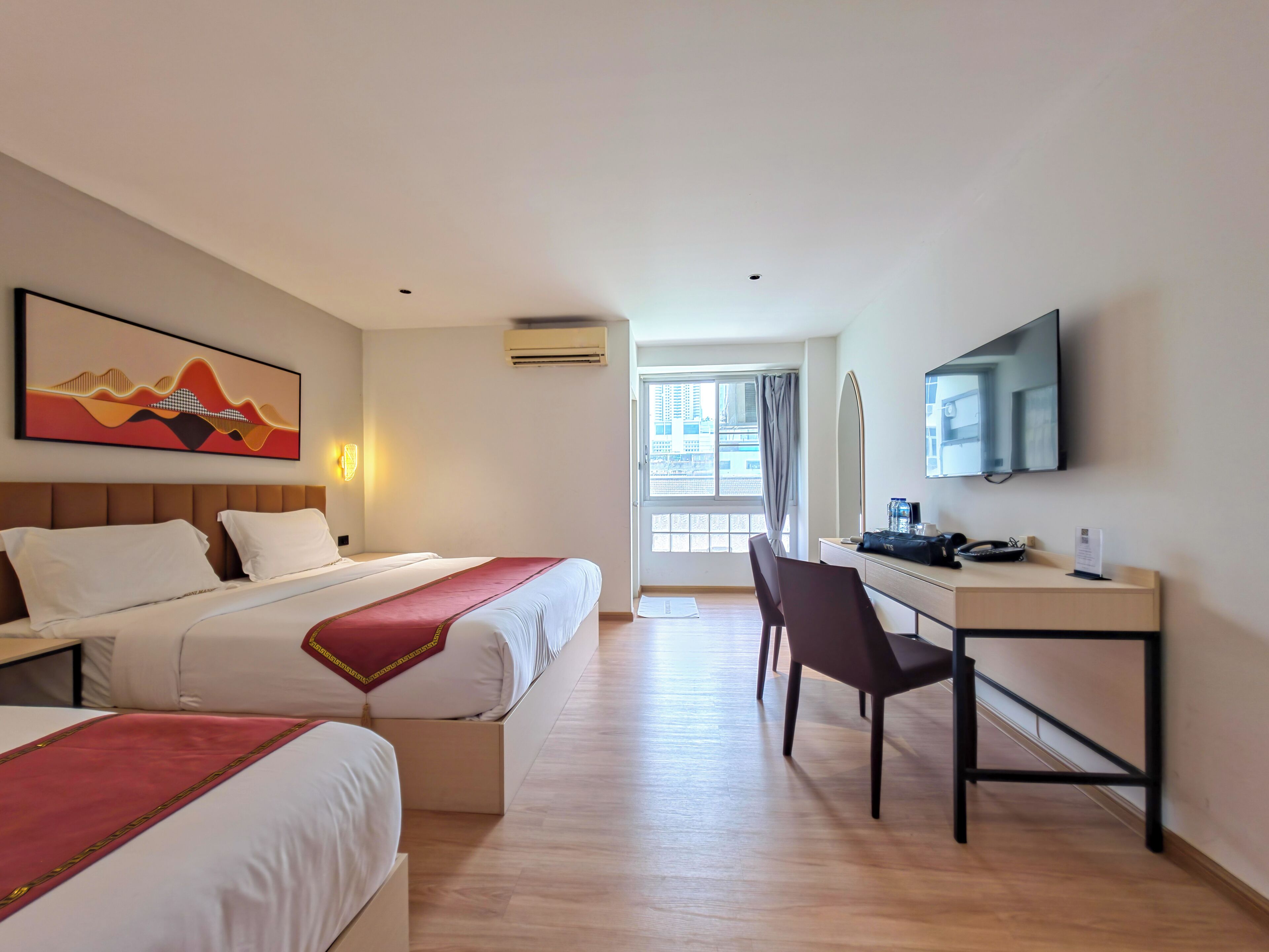 A hotel room with two beds, a desk, a chair, a TV, and a window with a view of buildings.