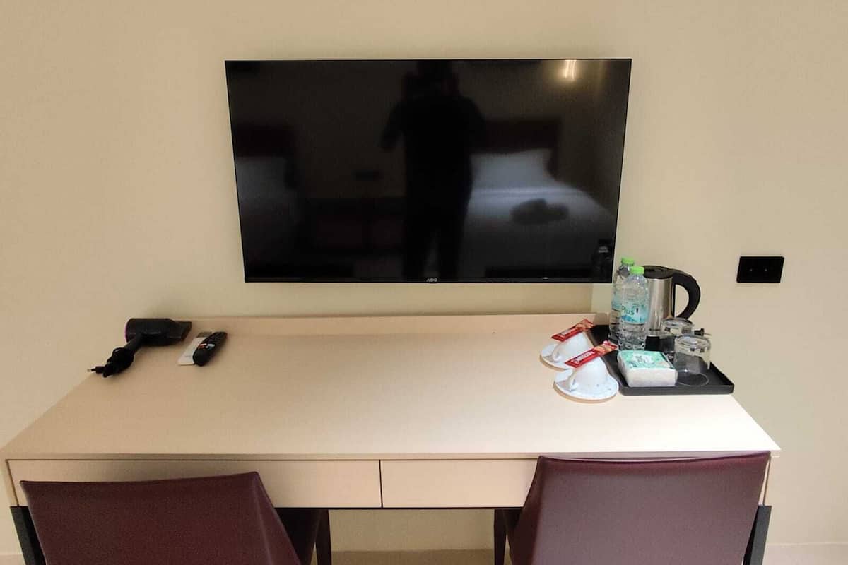 Habitación de hotel con un televisor de pantalla plana grande montado en la pared, un escritorio con teléfono y una silla.