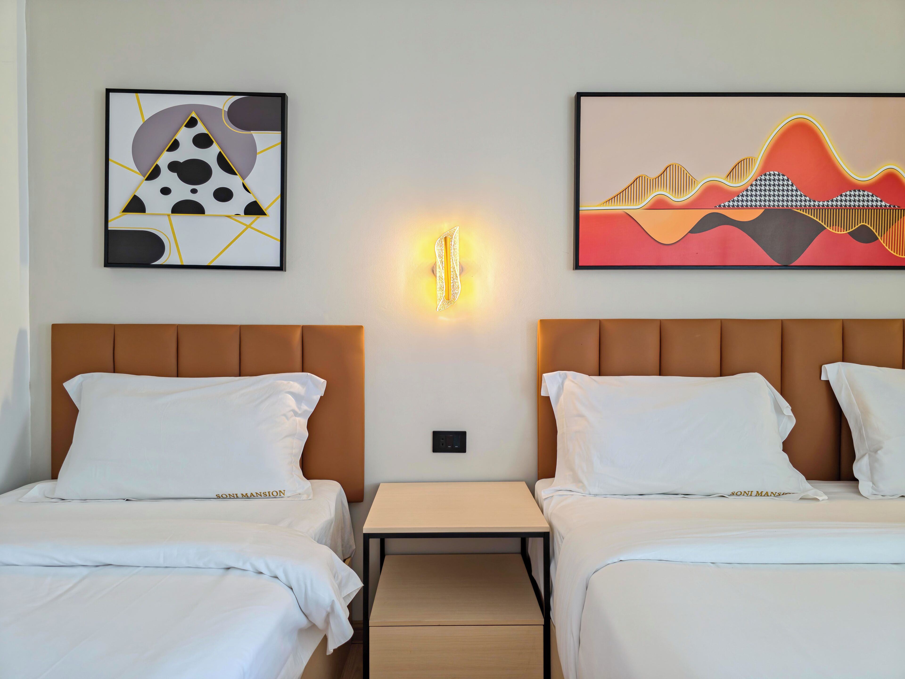 Une chambre d’hôtel avec deux lits, une table de chevet et des œuvres d’art accrochées aux murs.