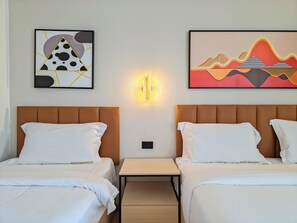 A hotel room with two beds, a nightstand, and artwork on the walls. - Hotel Soni Mansion Pratunam (Bangkok)