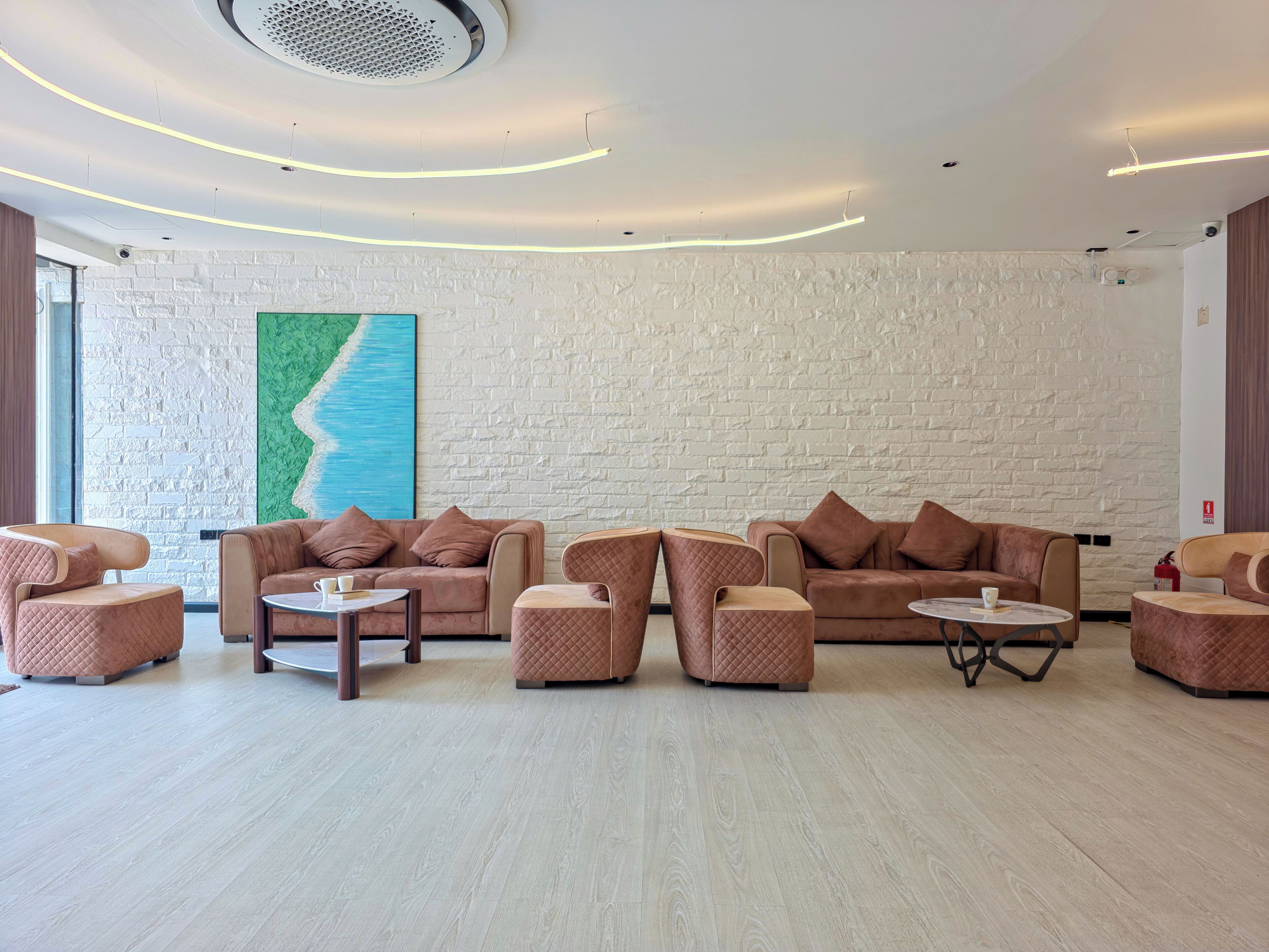 Un espace de détente moderne avec un mur en briques blanches, une grande peinture abstraite et un aménagement comprenant des canapés et des poufs.