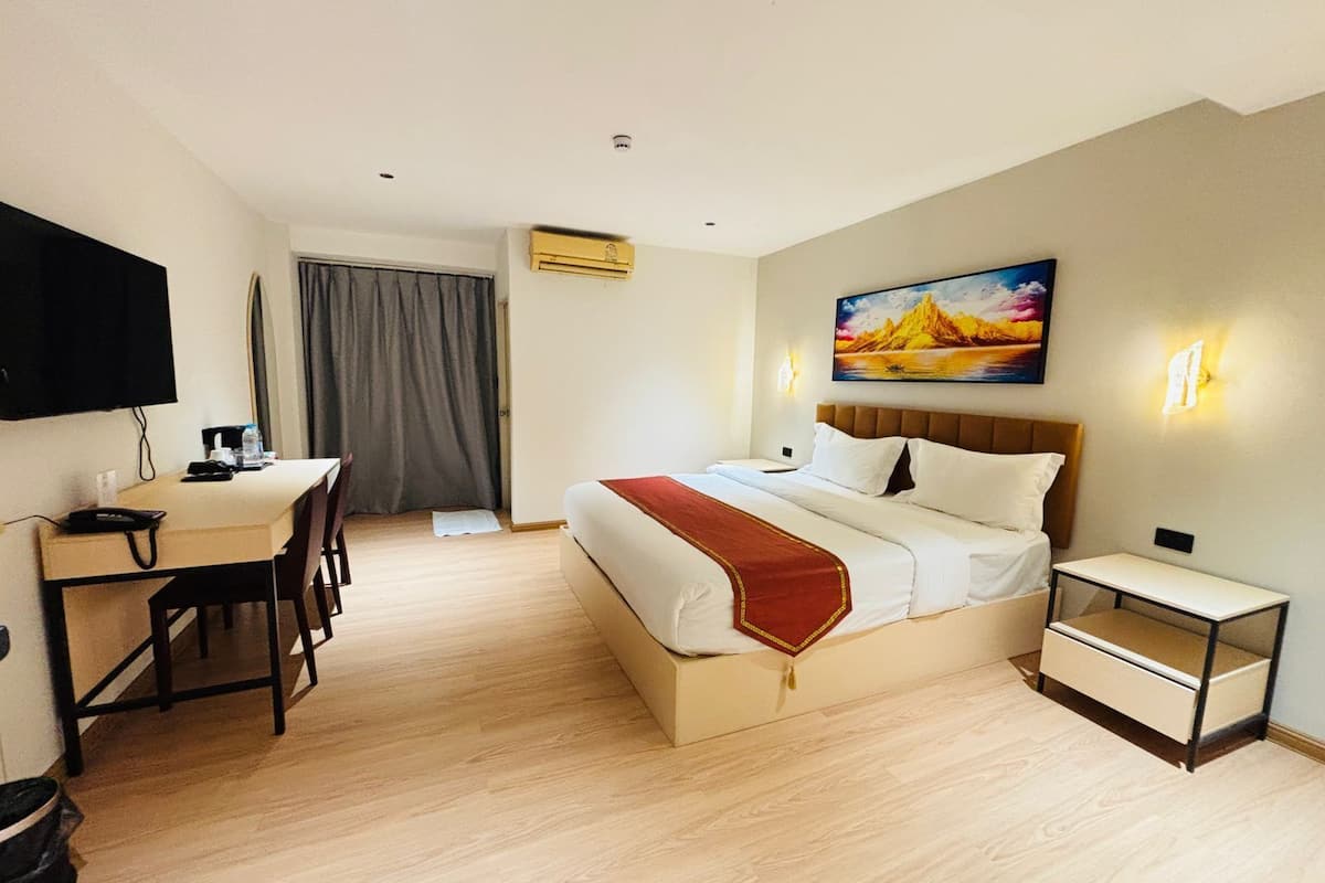 Una habitación de hotel con cama, mesita de noche, escritorio, silla y un cuadro en la pared.