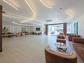 Eine geräumige Lobby mit modernen Möbeln, einem großzügigen Sitzbereich und Blick auf die Straße durch Glastüren.