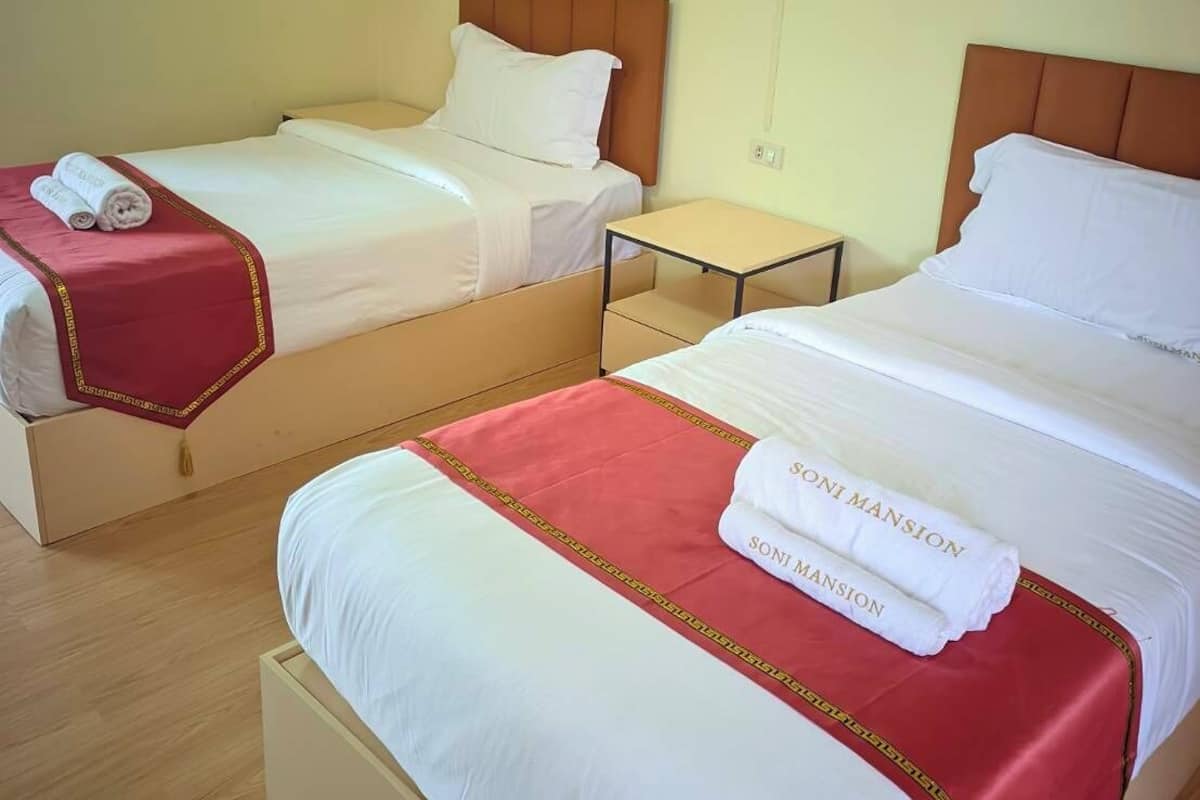 Habitación de hotel con dos camas, una mesita de noche pequeña y aire acondicionado de pared.