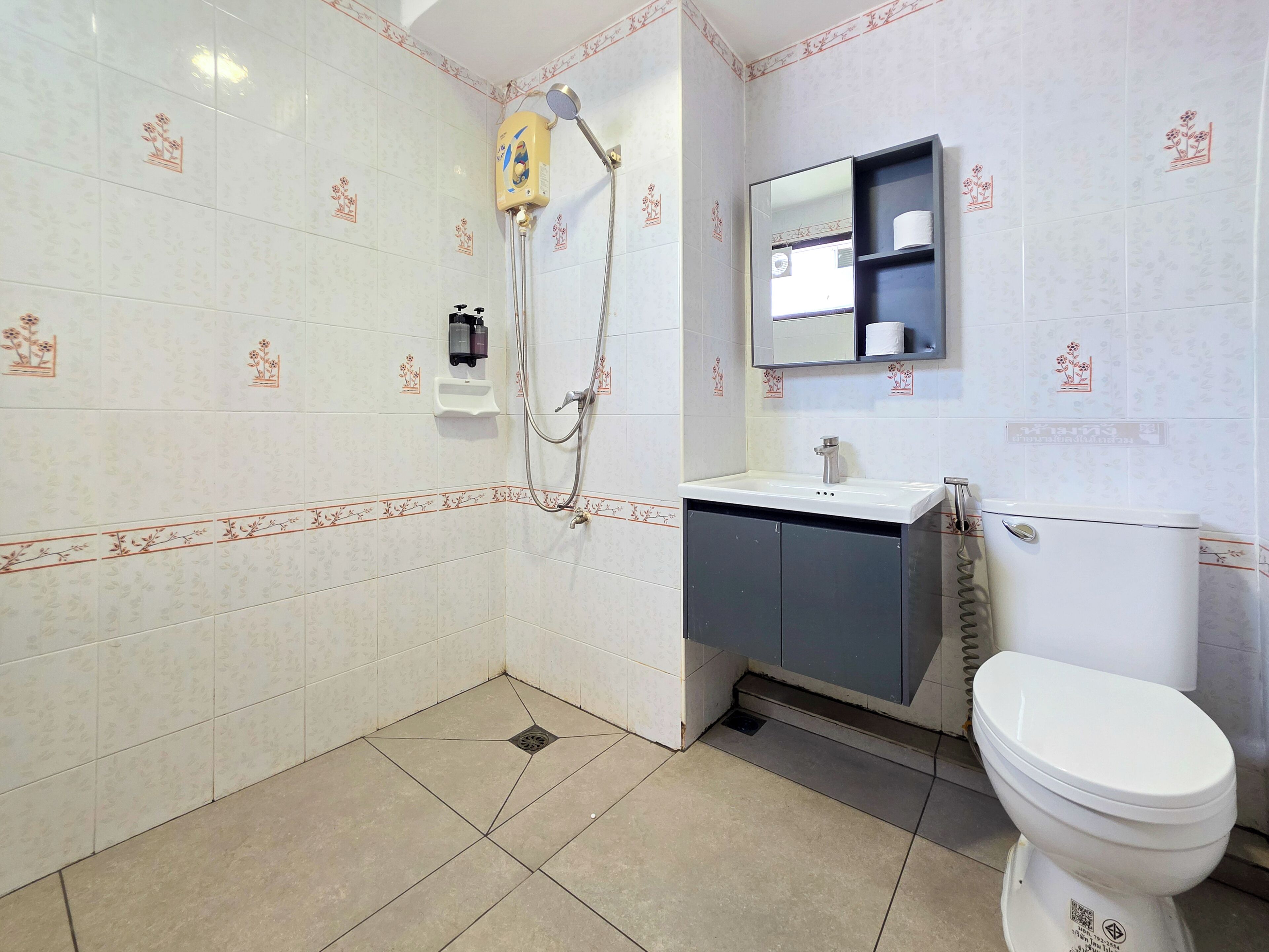 A bathroom with a toilet, sink, mirror, shower, and a toilet paper holder.