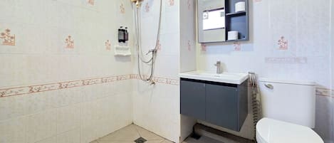Un baño con inodoro, lavamanos, espejo, ducha y un dispensador de papel higiénico.