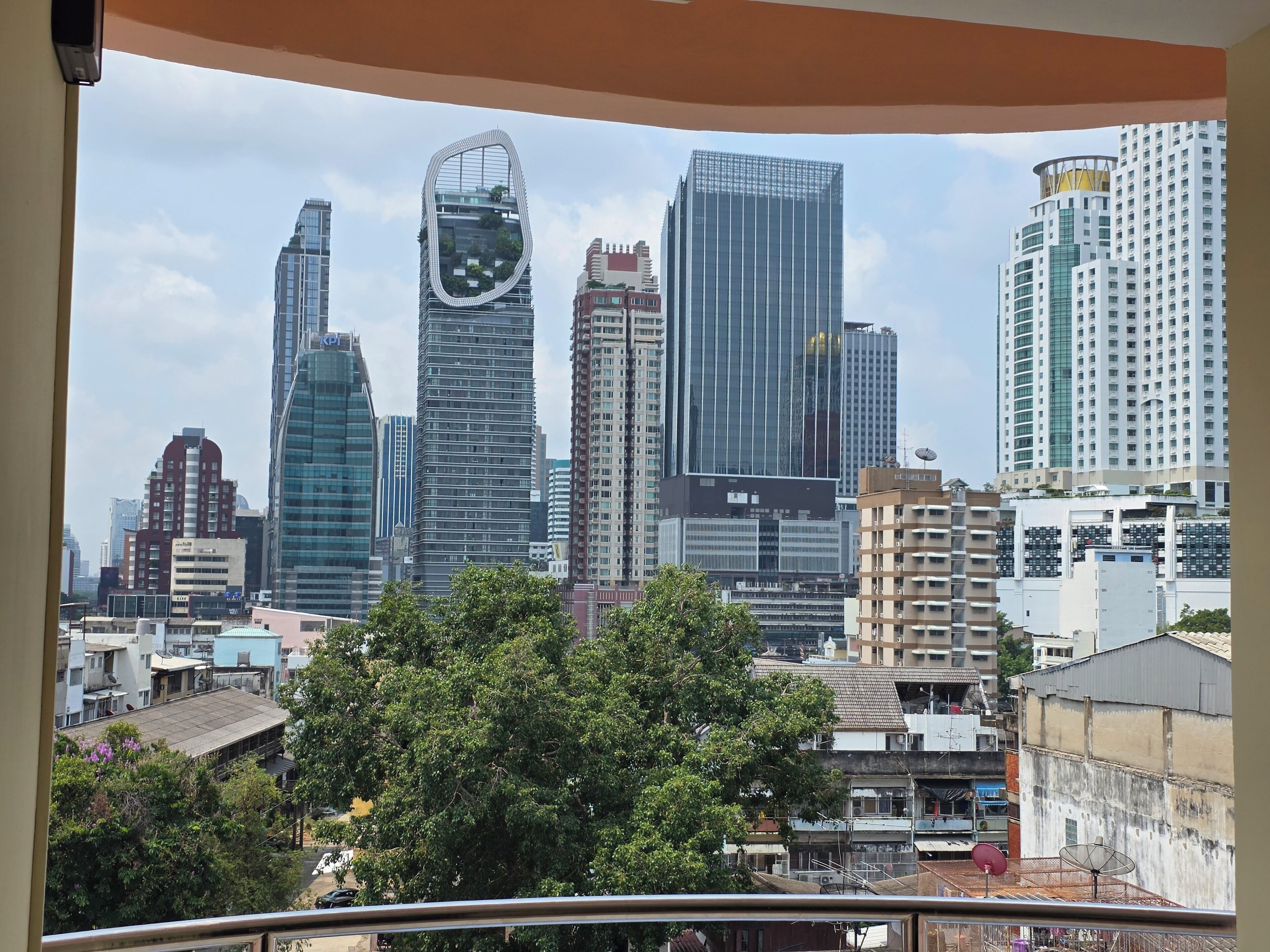Un paisaje urbano con edificios modernos de gran altura, una combinación de estructuras residenciales y comerciales, y un primer plano arbolado.