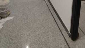 A hallway with a tiled floor, a black door, and a white wall with a small window. - Treebo Sai Village Suites (Gurugram)