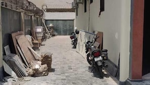 A narrow alleyway with construction materials and a parked motorcycle. - Treebo Sai Village Suites (Gurugram)