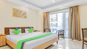 A hotel room with a large bed, a nightstand, a chair, and a view of the outside. - Treebo Sai Village Suites (Gurugram)