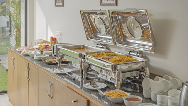 A buffet setup with various dishes and utensils. - Treebo Sai Village Suites (Gurugram)