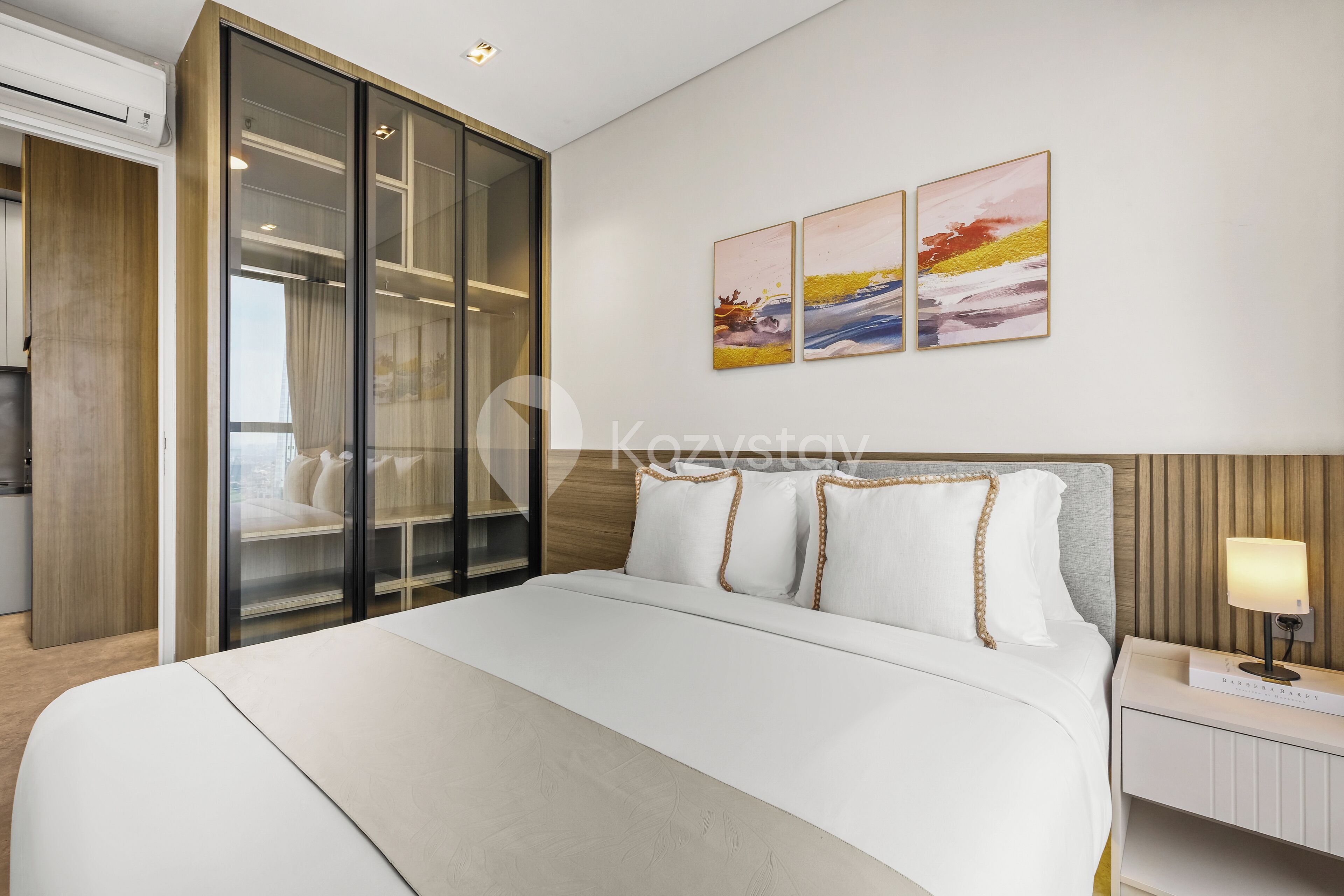 A modern hotel room with a large bed, a wardrobe with sliding doors, and a bedside table with a lamp.