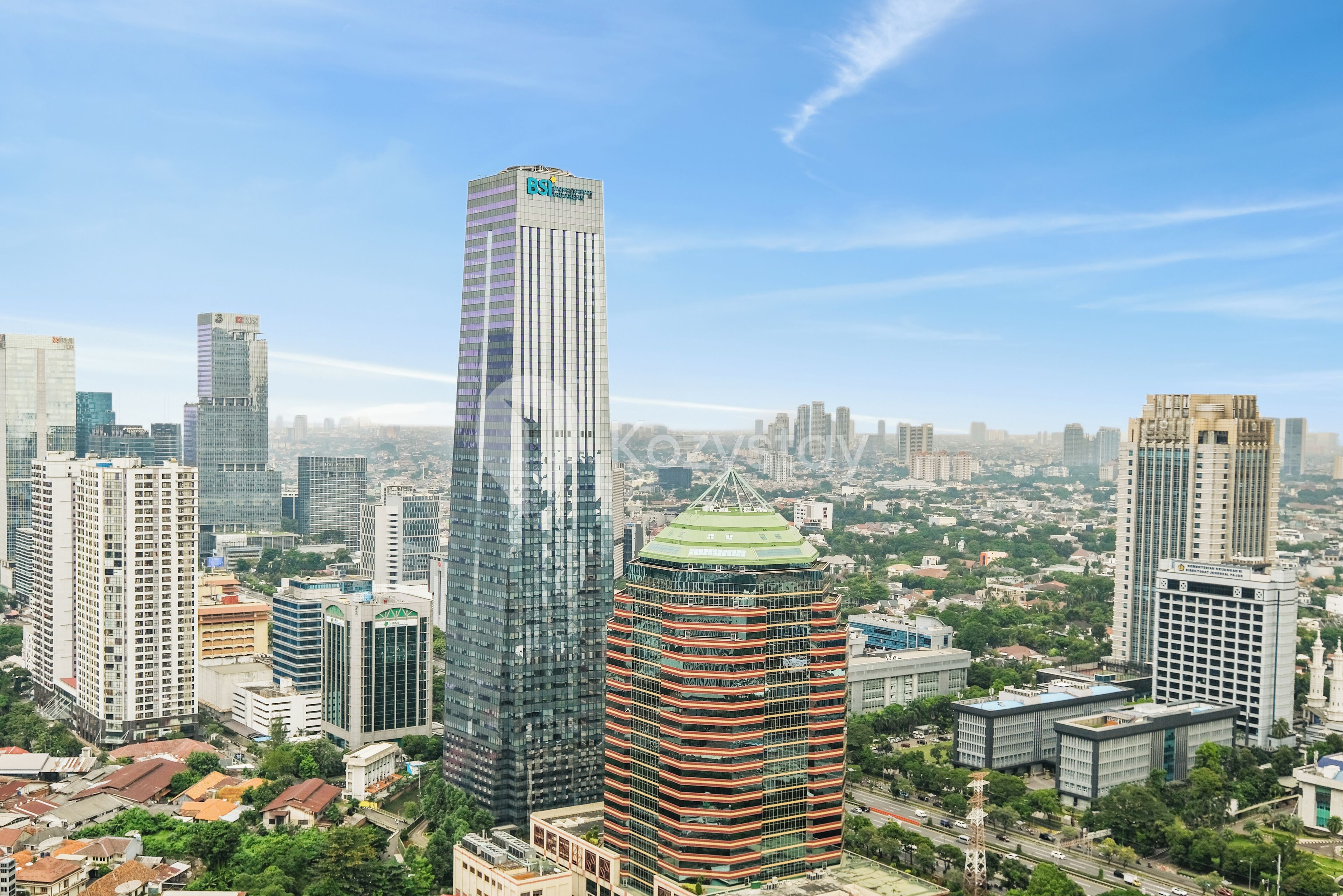 A high-rise building with a glass facade and a green rooftop, surrounded by other tall buildings and greenery.
