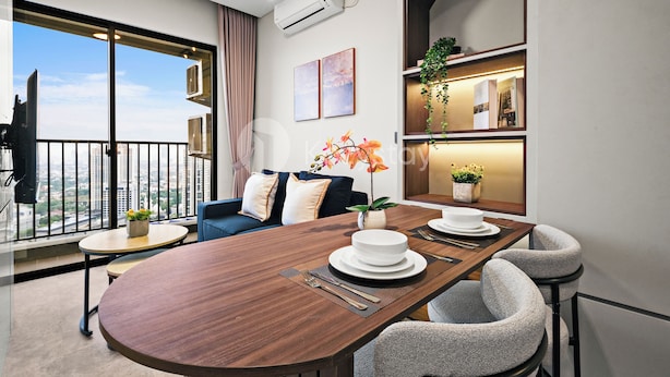 A modern living room with a wooden dining table, two sofas, a balcony with a view, and a kitchen area with a plant. - Havari by Kozystay - Sudirman (Jakarta)