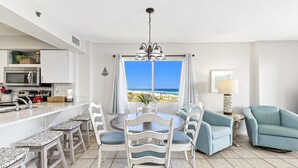 A modern kitchen with a large island, white bar stools, and a dining table with chairs. - Four Winds 301 (Orange Beach)