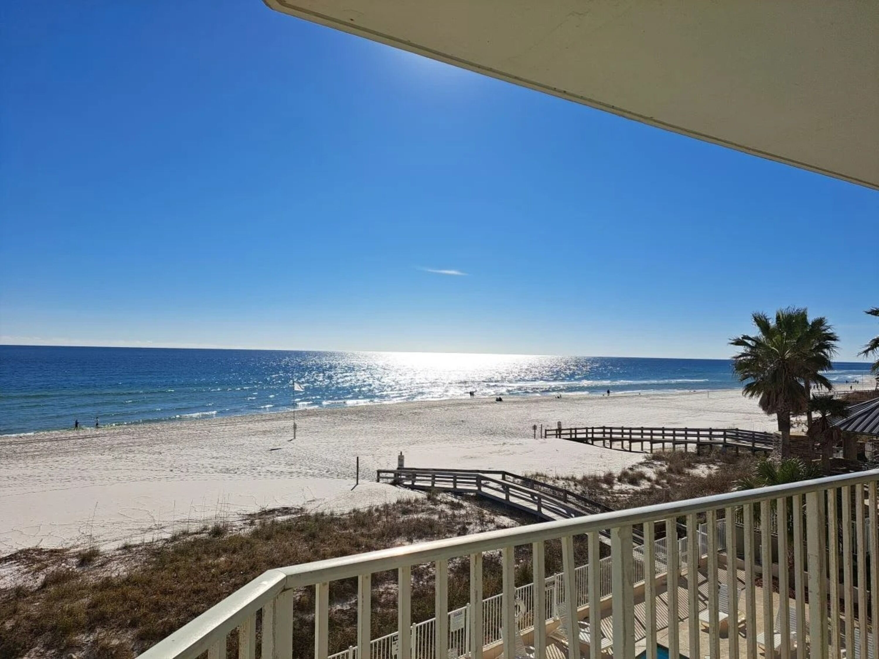 A beach view from a balcony with a wooden deck and palm trees.