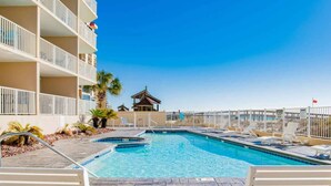 A swimming pool with lounge chairs, a palm tree, and a building with balconies. - Four Winds 301 (Orange Beach)
