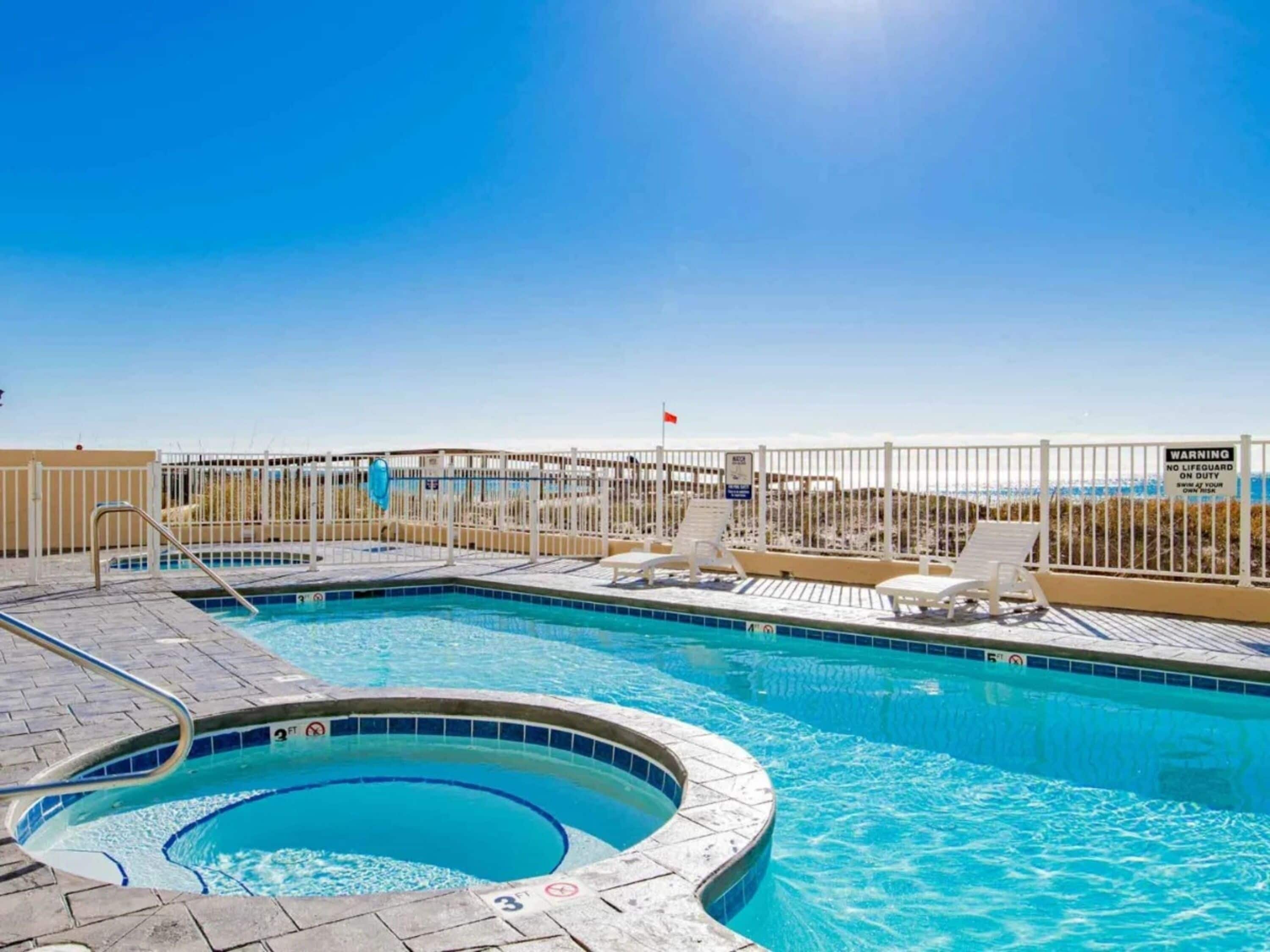 A swimming pool with a hot tub, lounge chairs, and a warning sign about no lifeguard on duty.
