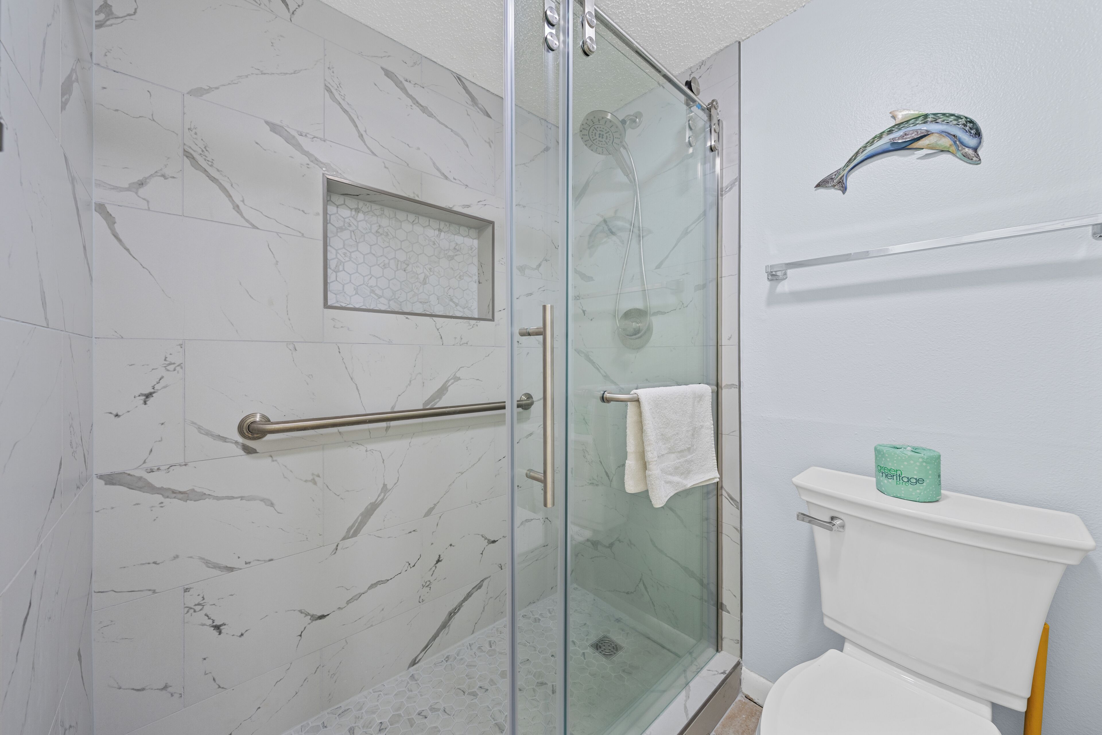 Une salle de bain avec une douche à parois de verre, des toilettes blanches et un porte-rouleau de papier toilette vert.