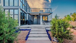 Ein modernes, zweistöckiges Haus mit überdachter Terrasse, Grill und Essbereich mit Gartenmöbeln.
