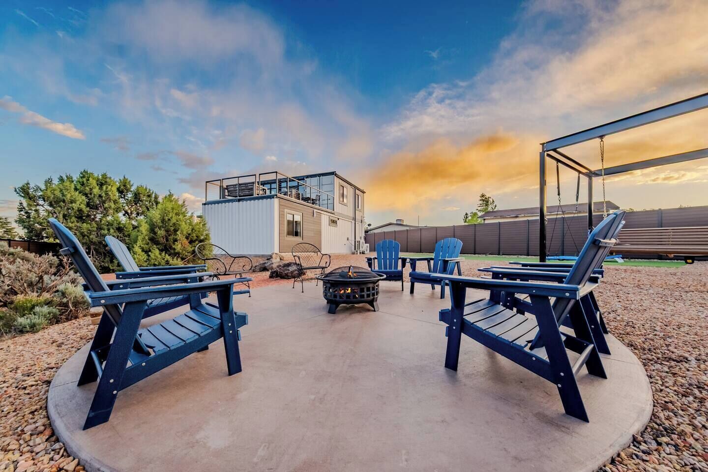 Une terrasse avec des fauteuils Adirondack, un foyer extérieur et un bâtiment doté d’un balcon.