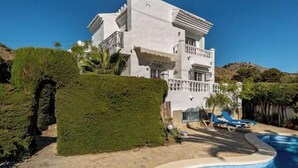 Una villa blanca con piscina, balcón y un sendero de piedra que lleva a la piscina.