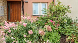 Un edificio residencial con puerta y ventanas de madera, rodeado de un jardín con diversas plantas en flor.