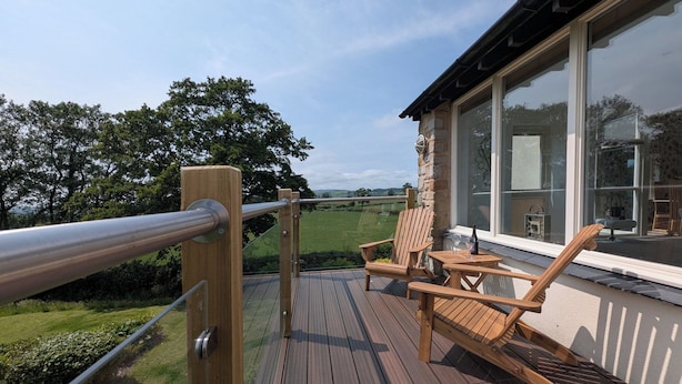 Una terraza de madera con barandilla de vidrio que da a un paisaje verde.