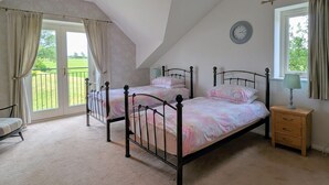 Un dormitorio con dos camas, una ventana con cortinas, una mesita de noche y vistas a un paisaje verde.