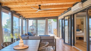 A modern interior with a wooden ceiling, large windows, a dining area with a table and chairs, and a view of the outdoors. - MH Holiday Dream - Shining Sea - Oaza Mira campsite (Drage)