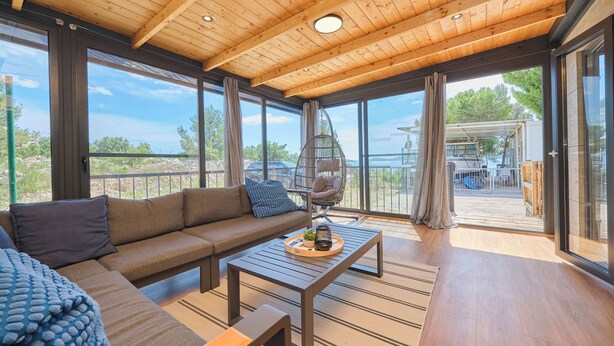A modern interior with a wooden ceiling, large windows, a sofa, a coffee table, and a hanging chair. - MH Holiday Dream - Shining Sea - Oaza Mira campsite (Drage)