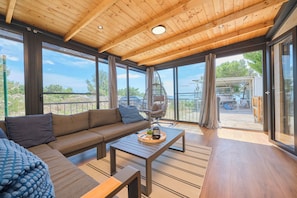 A modern interior with a wooden ceiling, large windows, a sofa, a coffee table, and a hanging chair.