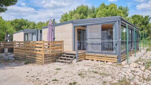 A modern cabin with a wooden deck, large windows, and a view of the surrounding forest. - MH Holiday Dream - Shining Sea - Oaza Mira campsite (Drage)