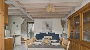 Een eetruimte met een tafel voor vier personen, een houten kast met glazen deuren en een plafond met zichtbare balken.