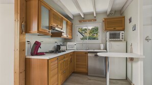 Een compacte keuken met houten kastjes, een gasfornuis, een magnetron en een vaatwasser.