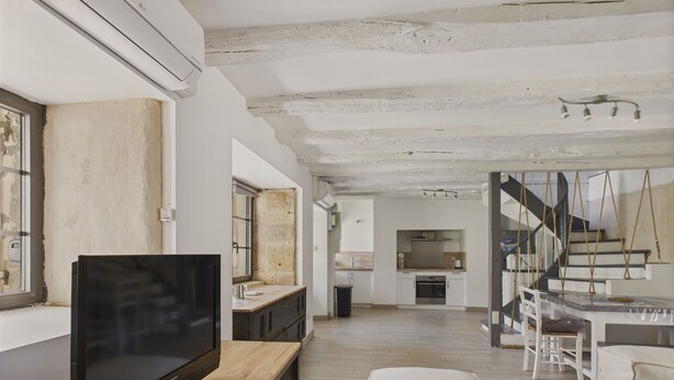 Ein moderner Wohnraum mit einem Flachbildfernseher auf einem Holztisch, einer Couch und einer Treppe, die zu einer erhöhten Ebene führt.