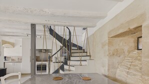 Ein Essbereich mit großem Tisch, der mit Plastikfolie abgedeckt ist, eine Treppe mit einer Taue und eine Küche im Hintergrund.