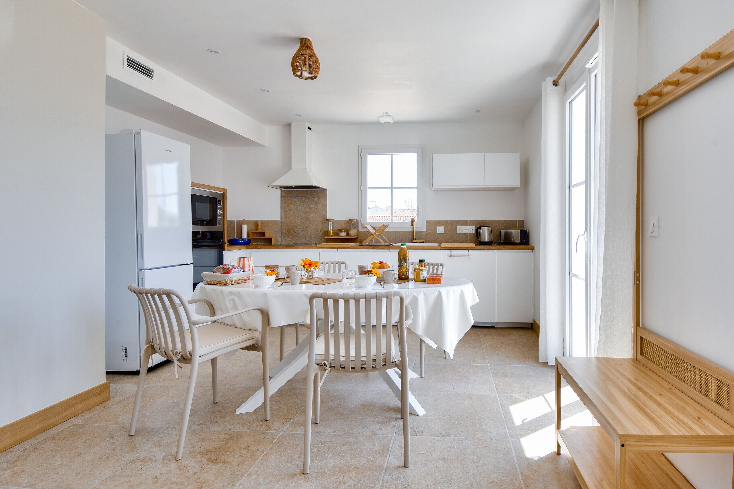 Une cuisine moderne avec des meubles blancs, un four encastré et un coin repas avec une table dressée pour quatre personnes.