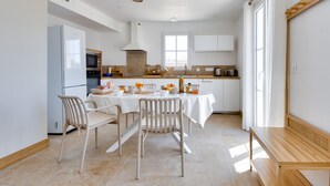 A modern kitchen with white cabinetry, a built-in oven, and a dining area with a table set for four. - House for 6, garden & AC, walk everywhere (Barbâtre)