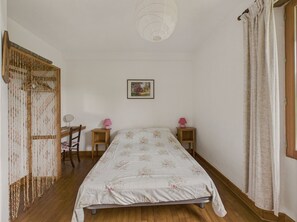 Un dormitorio con una cama, dos mesitas de noche, una silla, una lámpara colgante y una puerta con cortina.