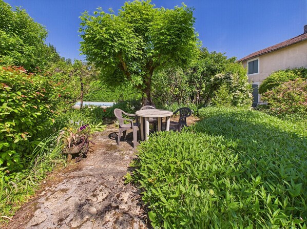 Stroll along the winding stone path to a secluded seating area surrounded by lush greenery and a majestic tree.