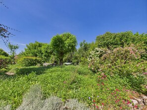 Relax in a serene garden setting surrounded by lush greenery and vibrant flowers, with a stone bench and a majestic tree providing shade.