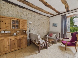 Relax in this charming room with a stone wall, wooden beams, and a comfortable armchair by the window.