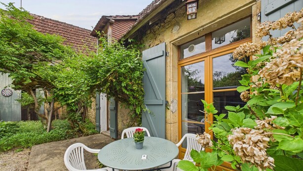 A rustic building with a wooden door, a small table with chairs, and a garden area with plants and a fence. - Shared pool and wooded grounds - house for 4 (Montignac)